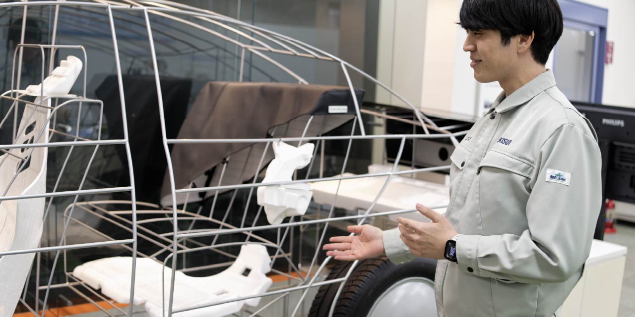 自動車のワイヤーフレーム模型に組み込まれたピオセラン製部材の前で説明する技術者